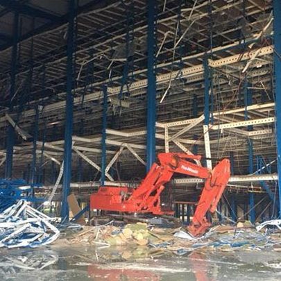 Bagger in einem Bauwerk mit Stahlgerüst und Bauresten im Vordergrund.