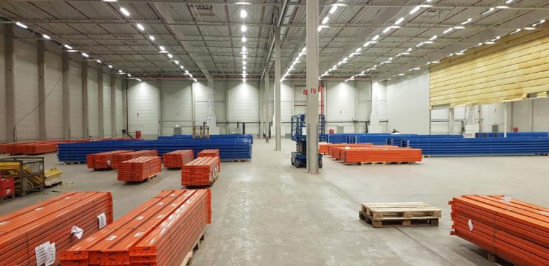 Große Lagerhalle mit orangefarbenen und blauen Containern, gut beleuchtet.