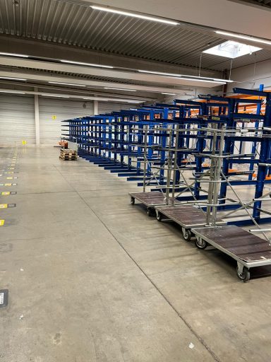 Lange Metallregale in einer Lagerhalle, auf Rollen, Boden grau.