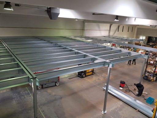 Blick auf ein Gerüst in einer Lagerhalle, mit Menschen und Maschinen im Hintergrund.