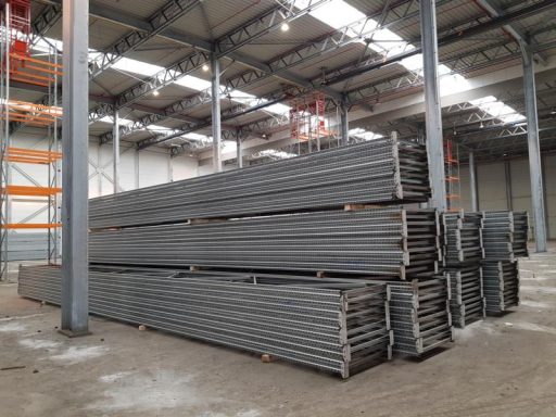 Lagerung von grauen Stahlträgern in einem großen Industriegebäude.